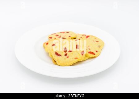 Ein Haufen traditioneller, knuspriger Scheiben und gebackener Plätzchen, hausgemachte goldene Kekse mit Stücken roter Kirsche auf einem weißen Teller Stockfoto