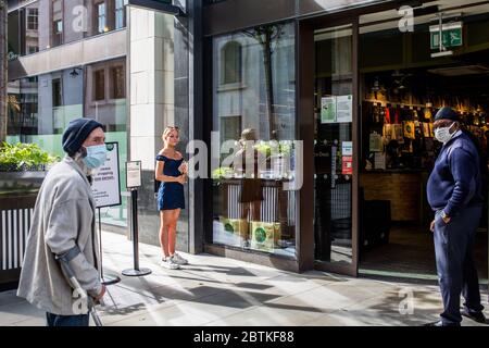 London, Großbritannien, 26. Mai 2020 inmitten der Coronavirus-Pandemie. Die Leute warten darauf, in den Supermarkt im Picadilly Circus zu gehen, während ein Wachmann zuschaut. Stockfoto