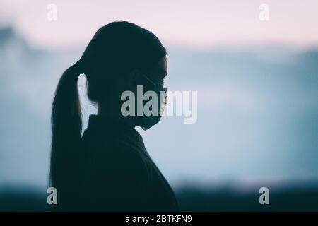 Coronavirus COVID-19 Angst psychische Gesundheit Problem traurige Frau trägt schützende medizinische Gesichtsmaske Silhouette allein Denken an die depressive Zukunft der Gesellschaft. Stockfoto