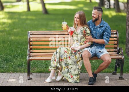 Fashion junge Teenager-Paar in einem Stadtpark mit Getränken sitzen auf einer Bank an einem sonnigen Sommertag ausruhen Stockfoto