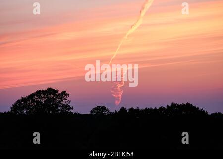 Ein Flugzeugabflug, der am Horizont bei Sonnenuntergang gesehen wird, während eines ungewöhnlich ruhigen Abends. Stockfoto