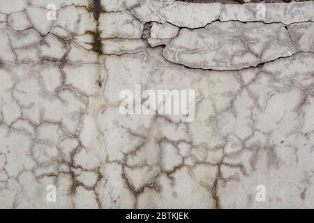 Beschädigte Betonwand mit großen Rissen. Textur der alten weißen Zementwand mit Rissen Stockfoto