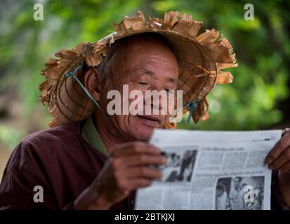 HOI AN - 10. MÄRZ 2018: Ein alter Mann mit einem asiatischen konischen Hut liest Zeitung draußen unter einer Straße auf der Straße in Hoi an, Vietnam am 10. März 2018 Stockfoto