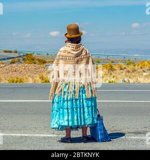 Bolivianische Aymara Indigene Frau wartet auf Transport entlang einer Autobahn, La Paz, Bolivien. Stockfoto