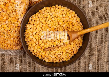 Gelbe Erbsen in einem Zellophanbeutel und Getreide in einer Keramikschale auf einem Hintergrund von grobstrukturiertem Burlap. Traditionelle Cerealien für die Herstellung von Suppen und Stockfoto