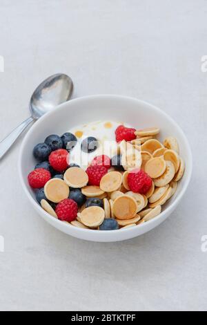 Schüssel mit hausgemachten Mini-Müsli Pfannkuchen mit Heidelbeeren Himbeeren Joghurt und Ahornsirup Stockfoto