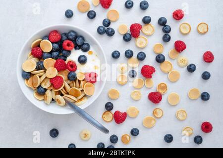 Schüssel mit hausgemachten Mini-Müsli Pfannkuchen mit Heidelbeeren Himbeeren Joghurt und Ahornsirup Stockfoto