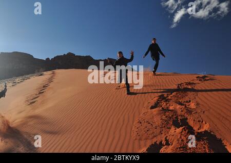 Kinder, die aus einer hohen Sanddüne in der Wüste Wadi RAM in Jordanien abstammen. Viel Spaß, wenn man in ein fernes Land reist. Stockfoto