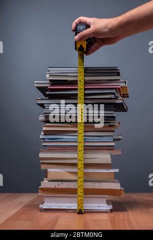 Hände einer Person, die die Größe eines Berges von Büchern, die die Informationen darstellen, misst Stockfoto