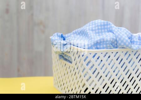 Blanke blau weiße Hemden in einem weißen Kunststoffkorb auf einem gelben Tisch auf grauem Hintergrund. Wäsche, Hausreinigung, Sauberkeit und Frische Stockfoto