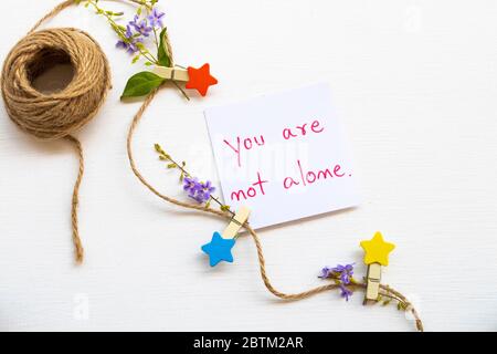 Sie sind nicht allein Message Card Handschrift mit Holzstern, Seil und lila Blumen Anordnung flach legen Postkarte Stil auf weiß Stockfoto