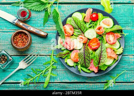 Salat mit gesalzenem Lachs, Gemüse und Kräutern auf einem alten Holztisch. Stockfoto