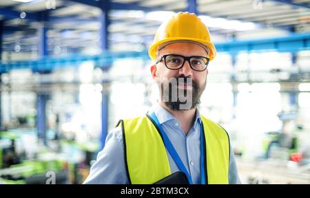 Vorderansicht des Technikers oder Ingenieurs mit Schutzhelm in Industriefabrik. Stockfoto