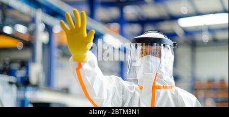 Arbeiter mit Schutzmaske und Anzug in Industriefabrik, Grußhandgeste. Stockfoto