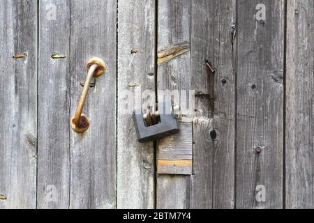 An der Holztür hängt ein altes eisernes Vorhängeschloss. Verschlossene Tür zum Raum. Konzept von Schutz, Inhaftierung, Schutz, Gefängnis. Stockfoto