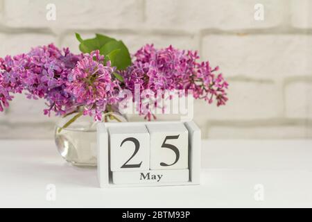 Mai 25 auf einem Holzkalender neben einem Strauß Flieder.ein Tag des Frühlingsmonats.Ende des Schuljahres.Letzter Anruf in der Schule. Stockfoto