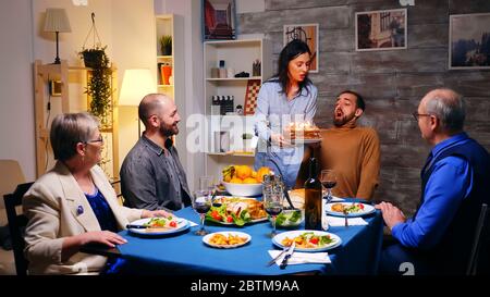 Folgen Sie Schuss von jungen Frau mit Geburtstagskuchen für ihren Bruder beim Familienessen. Stockfoto