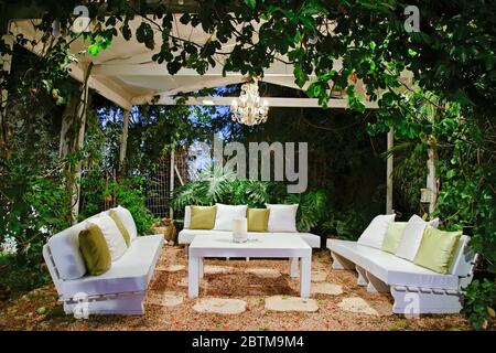 Terrasse romantisch am Abend mit Bänken und Kissen Kronleuchter und Tisch Stockfoto