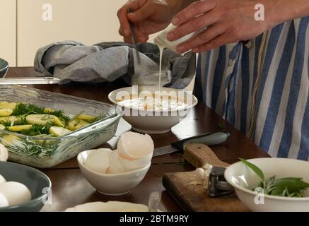 Hausmannskost, Frau schlägt Eier und Sahne für hausgemachte Kartoffelgratin Stockfoto