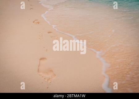 Fußspuren im Sand am Meer. Strand, Wellen und Fußspuren bei Sonnenuntergang, traumhafte Strandlandschaft, Wellen Stockfoto