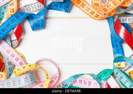 Haufen der bunten Maßbänder in Form von Rahmen auf Holz- Hintergrund. Blick von oben auf die schlanke Taille Konzept mit kopieren. Stockfoto