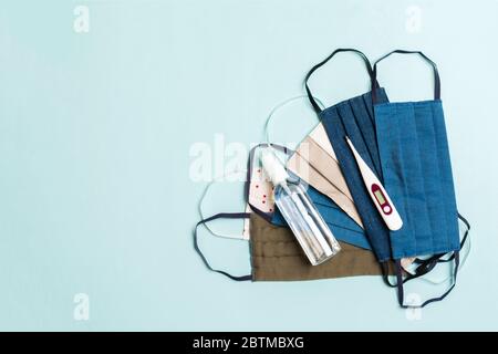 Draufsicht von handgefertigten Baumwollmasken, Digitalthermometer und Alkohol Gel Desinfektionsmittel auf blauem Hintergrund. Schutzausrüstung Konzept mit Kopierraum. Stockfoto