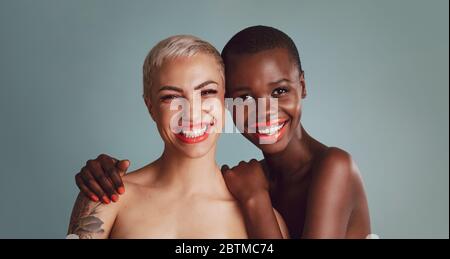 Porträt von zwei schönen jungen Frauen mit Make-up vor einem grauen Hintergrund. Weibliche Modelle mit kurzen Frisur Blick auf Kamera und lächeln zusammen Stockfoto