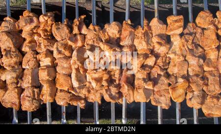 Frisches Fleisch, das auf Spieße gekleidet ist, wird auf einem Bräter oder Grill gebraten. Der Küchenchef bereitet Fleisch in einem Café oder Restaurant zu. Frisches rohes und gebratenes Schweinefleisch, Rind und Lamm Stockfoto
