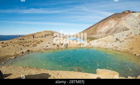 Gefrorene Emerald Lakes mit Felsen auf dem Eis, das von den Touristen geworfen wird, auf dem Tongariro Alpine Crossing in Neuseeland Stockfoto