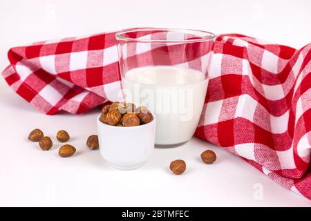 Glas von frischer veganer Haselnuss Milch rustikalen Stil. Ein Stapel Haselnüsse in einem weißen Becher und ein Glas mit frischer Milch auf Basis von weißen Nüssen. Stockfoto