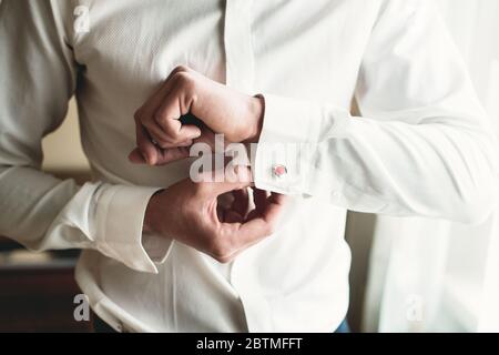 Ein Mann befestigt Manschettenknöpfe auf dem weißen Hemd. Nahaufnahme einer Männerhand mit einem weißen Hemd und Manschettenknöpfen. Stockfoto