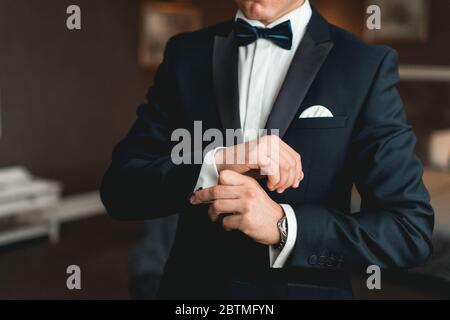 Ein Mann befestigt Manschettenknöpfe auf dem weißen Hemd. Nahaufnahme einer Männerhand mit einem weißen Hemd und Manschettenknöpfen. Stockfoto