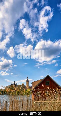 Bootshaus mit Schilf und Schweriner Schloss im Hintergrund. Vertikales Panorama mit Wolken und blauem Himmel. Stockfoto