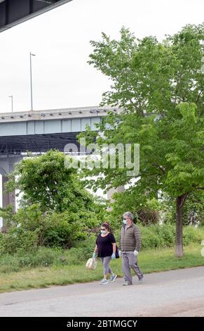 Ein Paar mittleren Alters gehen mit chirurgischen Masken. Im Little Bay Park in Queens, unter den Eingängen zur Throgs Neck Bridge. Stockfoto