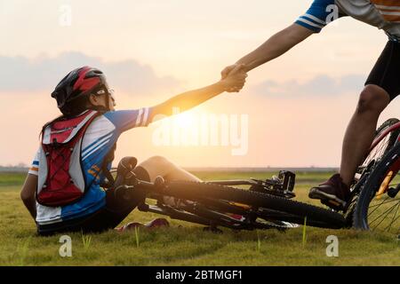 Frau Mountainbike fahren war Unfall abgestürzt und fiel auf das Gras, während ein Liebhaber ihr Kommen in die schöne Sonnenuntergang Zeit zu helfen. Verwenden von Hilfe und Stockfoto