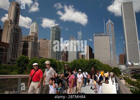 Horizontale Seitenansicht einiger Menschen, die die Renzo Piano Nichols Bridgeway überqueren, mit der Skyline von Chicago als Hintergrund, Millenium Park Stockfoto