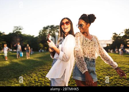 Schöne Mädchen in Sonnenbrille glücklich spielen auf wenig Gitarre und tanzen, während die Zeit zusammen im Park Stockfoto