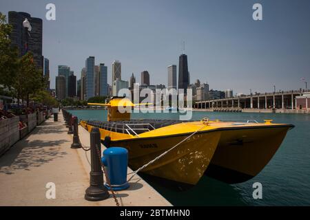 Horizontale sonnige Ansicht eines gelben Touristen-Katamarans, der am Navy Pier vor Anker liegt, mit der Skyline von Chicago im Hintergrund, einschließlich John Hancock Center Stockfoto