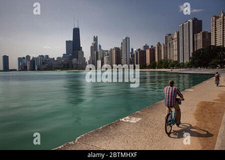 Horizontale Ansicht von zwei Personen, die am Michigan Lake Fahrrad fahren, mit der Skyline von Chicago im Hintergrund, North Ave Beach, Illinois, USA Stockfoto