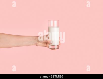 Mädchen Hand zeigt Glas voller Milch auf rosa Hintergrund, Nahaufnahme Stockfoto