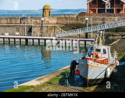 Newhaven, Edinburgh, Schottland, Großbritannien, 27. Mai 2020. UK Wetter: Reflexionen an einem warmen sonnigen Tag mit einem Fischerboot, das einen Rumpf mit einem starken Jet Spray sauber hält Stockfoto