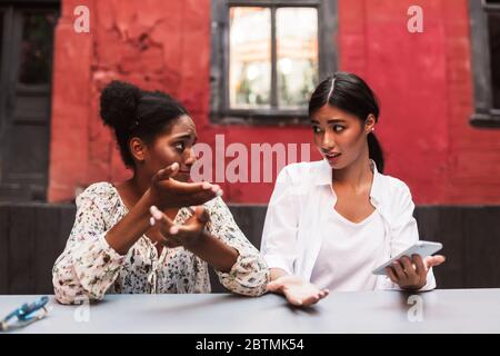 Zwei junge Frauen, die sich beim gemeinsamen Aufenthalt im Innenhof des Cafés verblüfft anguchten Stockfoto