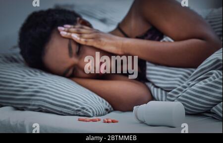 Pillen aus Glas auf dem Bett bestreut, kann afroamerikanische Mädchen nicht einschlafen Stockfoto