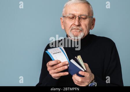 Alter attraktiver Mann mit grauen Haaren und Bart in Brillen und Pullover nachdenklich halten Tickets und Pässe in Händen über blauem Hintergrund Stockfoto