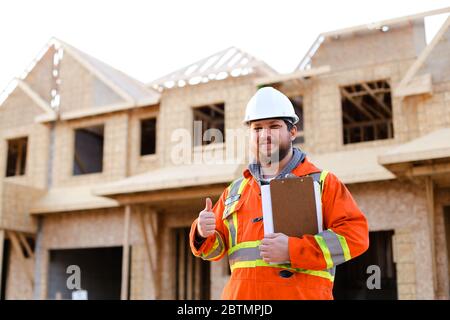 Vorarbeiter in orangefarbener Wrokwear, der das Notizbuch hält und die Daumen nach oben zeigt. Stockfoto