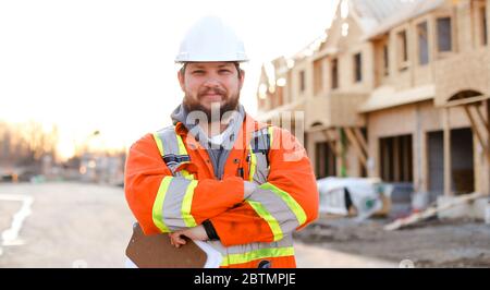 Kaukasischer Vorarbeiter in orangefarbener Arbeitskleidung, der das Notizbuch auf der Baustelle hält. Stockfoto