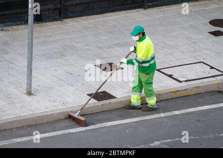 Straßenfeger trägt Gesichtsmaske arbeiten auf einem Bürgersteig. Öffentliches Reinigungskonzept während der Coronavirus-Pandemie Stockfoto