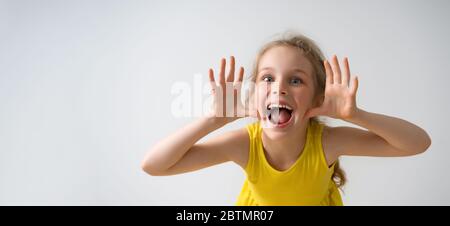 Sly glücklich Vorschule Mädchen in sonnigen gelben Kleid neckt jemand, schreien und lachen mit einem lustigen Gesicht. Nahaufnahme Studio isoliert auf weiß Stockfoto