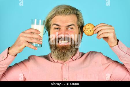 Bärtiger Mann trinkt Milch mit Plätzchen. Lassen Sie es für Santa. Frühstück oder Mittagessen. Milch und süße Kekse. Happy Hipster essen Plätzchen Dessert. Köstliche Leckereien. Hausgemacht ist am besten. Rezept zum Backen von Plätzchen. Stockfoto