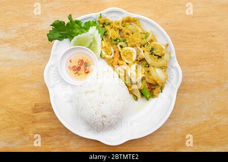 Gebratener Tintenfisch in Currypulver mit Reis und Fischsauce gemischt Chili in weißer Schüssel auf Holztisch rühren. Stockfoto